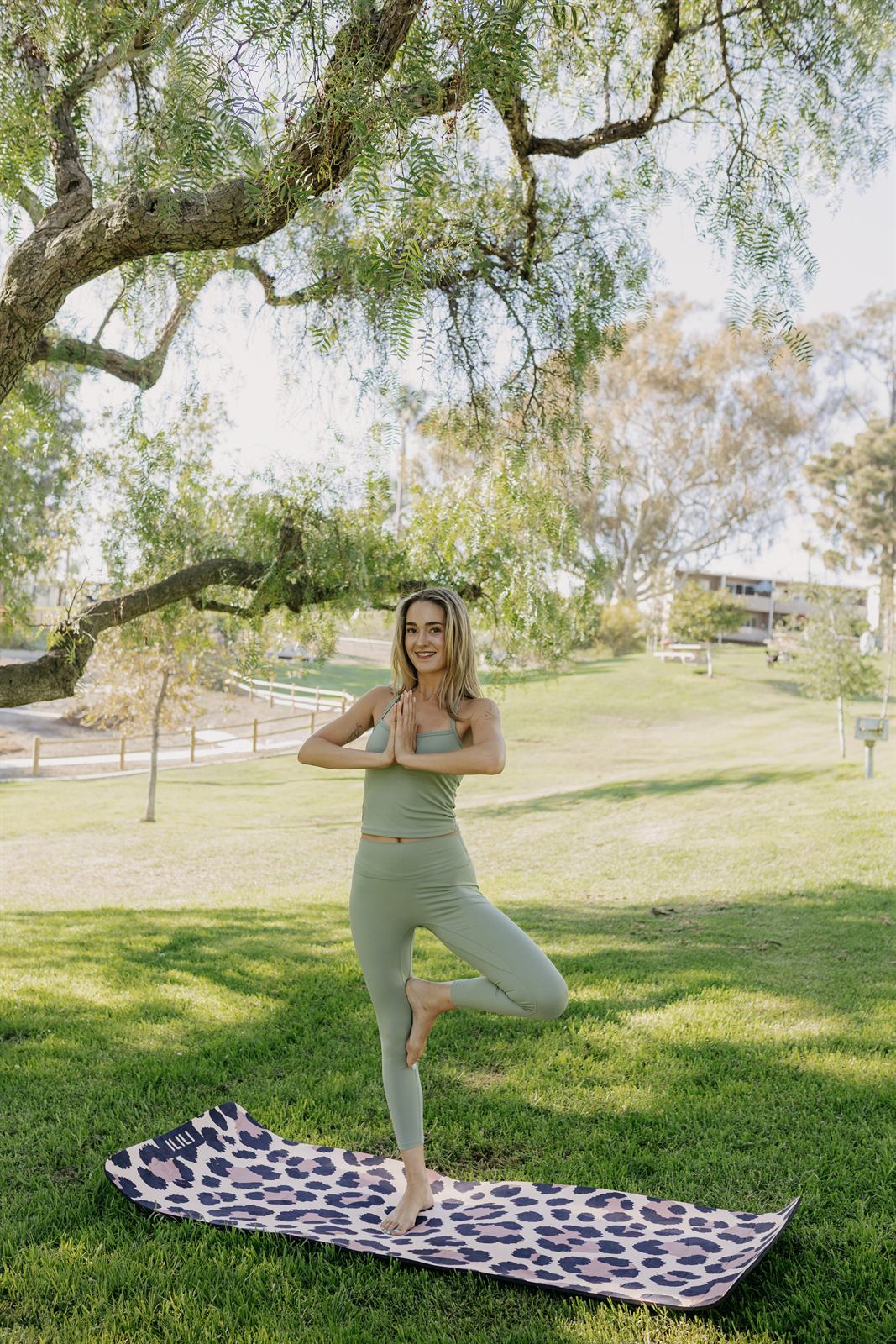 Teacher balancing in tree pose on a mat in the grass