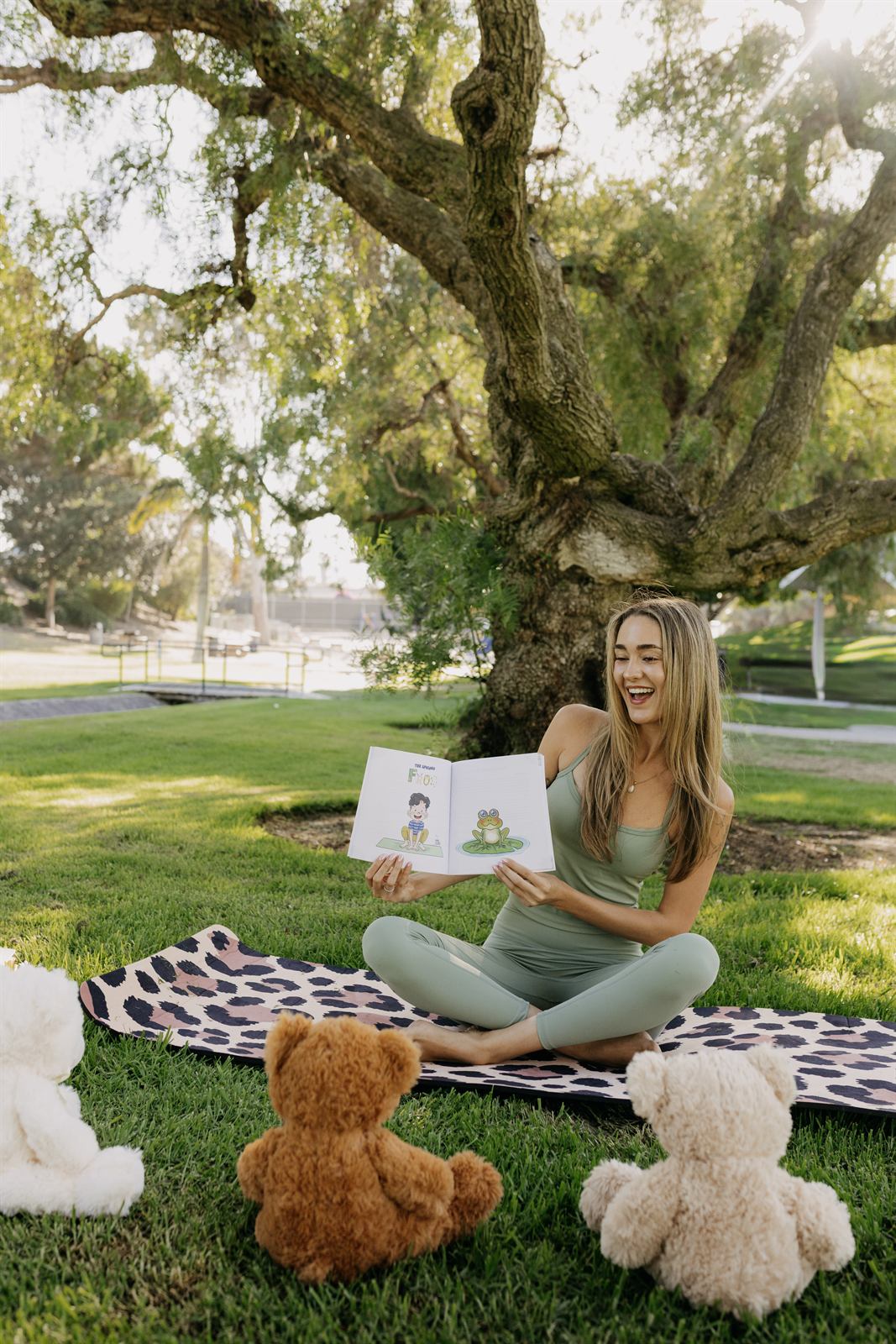 Teacher seated under a tree with a book and teddy bears
